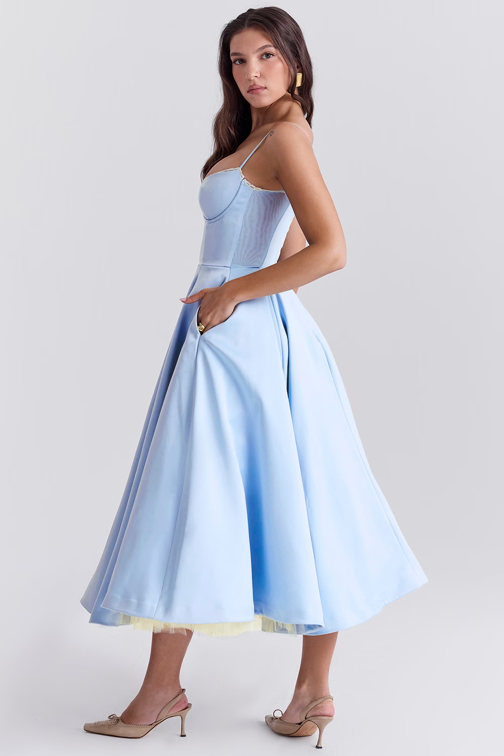 Frau in hellblauem, schulterfreiem Abendkleid mit weitem Rock und Spaghettiträgern, seitlich stehend, elegante Mode, Studioaufnahme.