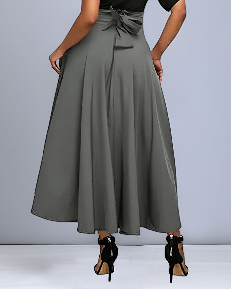 Frau in grauem, knöchellangem A-Linien-Rock mit Schleife, schwarze High Heels. Elegante Damenmode, stilvoller Rock, modische Kleidung.