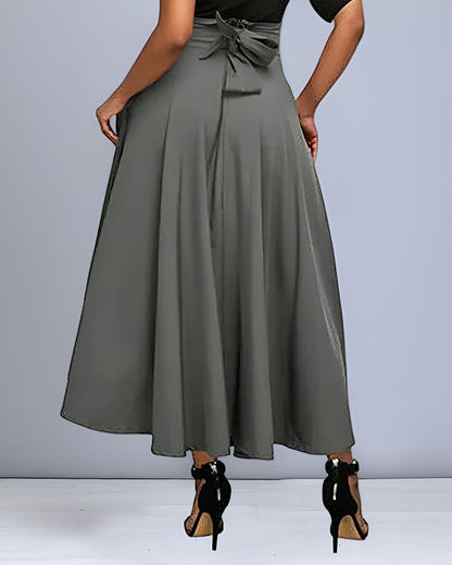 Frau in grauem, knöchellangem A-Linien-Rock mit Schleife, schwarze High Heels. Elegante Damenmode, stilvoller Rock, modische Kleidung.