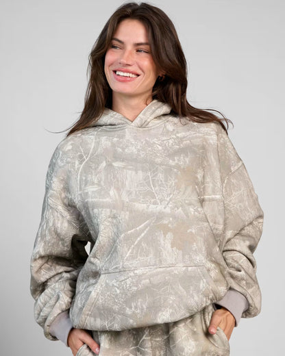 Frau in grauem Camouflage-Hoodie lächelt, lässige Mode, Herbst-Outfit, gemütlicher Kapuzenpullover, Streetwear-Trend, stilvolle Damenbekleidung.