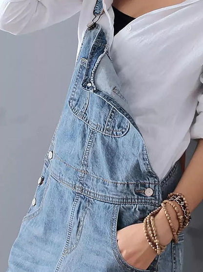 Damenmode: Frau in weißer Bluse und blauer Jeans-Latzhose, trägt Armbänder. Trendige Freizeitkleidung, lässiger Stil, modisches Outfit.