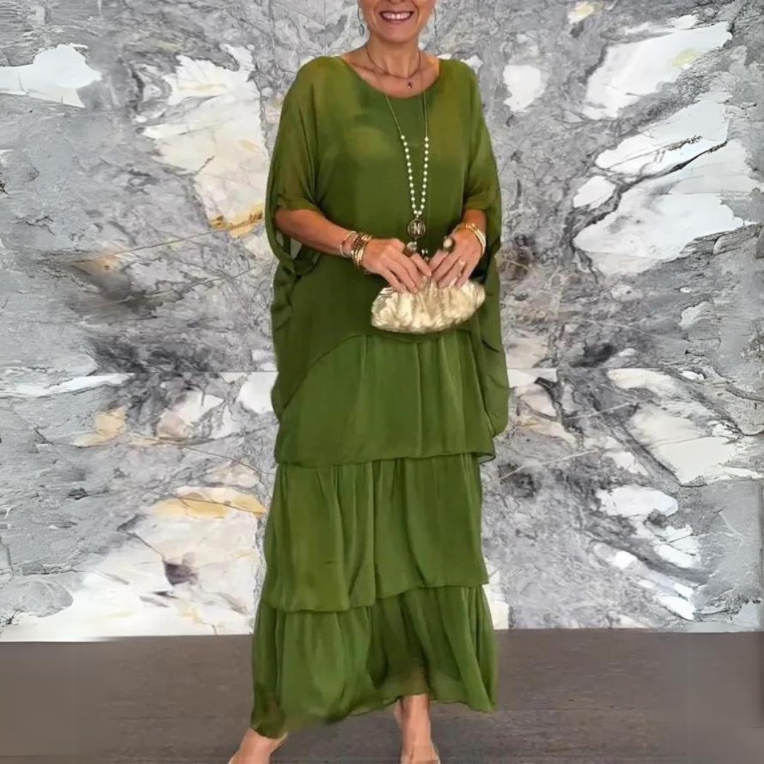 Elegante Frau in grünem Maxikleid vor marmorierter Wand, hält goldene Clutch. Mode, Abendkleid, stilvoll, Damenmode, Accessoires.