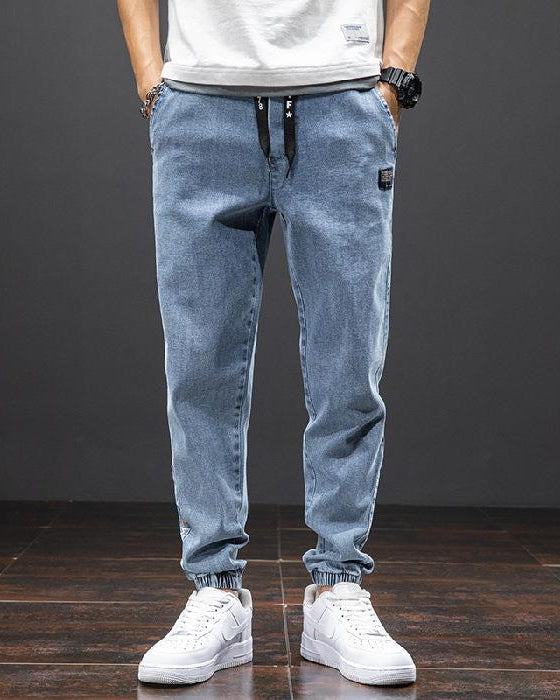 Mann trägt blaue Jeans-Jogginghose und weiße Sneakers, lässiger Stil, Mode für Herren, bequeme Freizeitkleidung, moderne Streetwear.