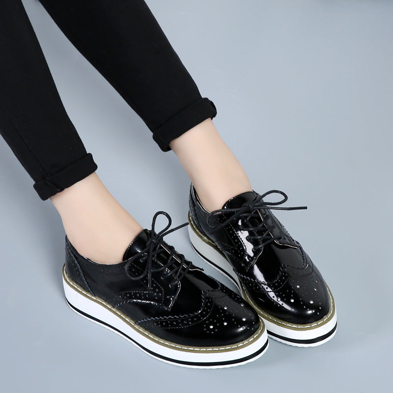 Schwarze Lackleder-Brogues mit weißer Plateausohle, getragen von Person in schwarzer Hose. Modische Damen-Schuhe, elegantes Design, trendiger Look.