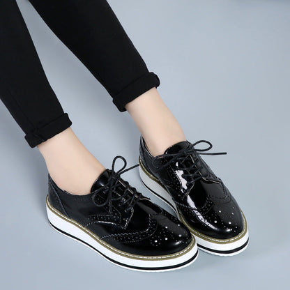 Schwarze Lackleder-Brogues mit weißer Plateausohle, getragen von Person in schwarzer Hose. Modische Damen-Schuhe, elegantes Design, trendiger Look.