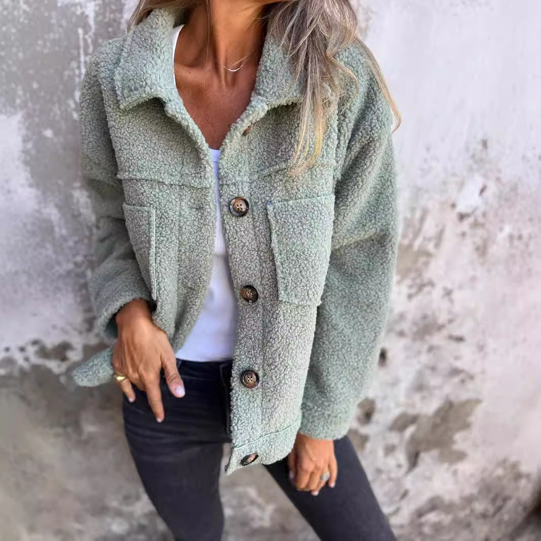 Dame in grüner Teddyjacke, weißem Shirt und schwarzer Jeans vor Betonwand. Modetrend, Herbstmode, lässiger Stil, Damenbekleidung.