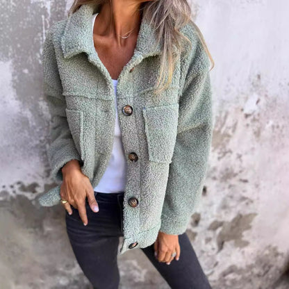 Dame in grüner Teddyjacke, weißem Shirt und schwarzer Jeans vor Betonwand. Modetrend, Herbstmode, lässiger Stil, Damenbekleidung.