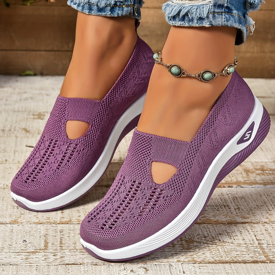 Lila Damen-Sneaker mit Strickmuster, weißer Sohle und Logo, getragen mit Jeans und türkisfarbenem Fußkettchen auf Holzboden.