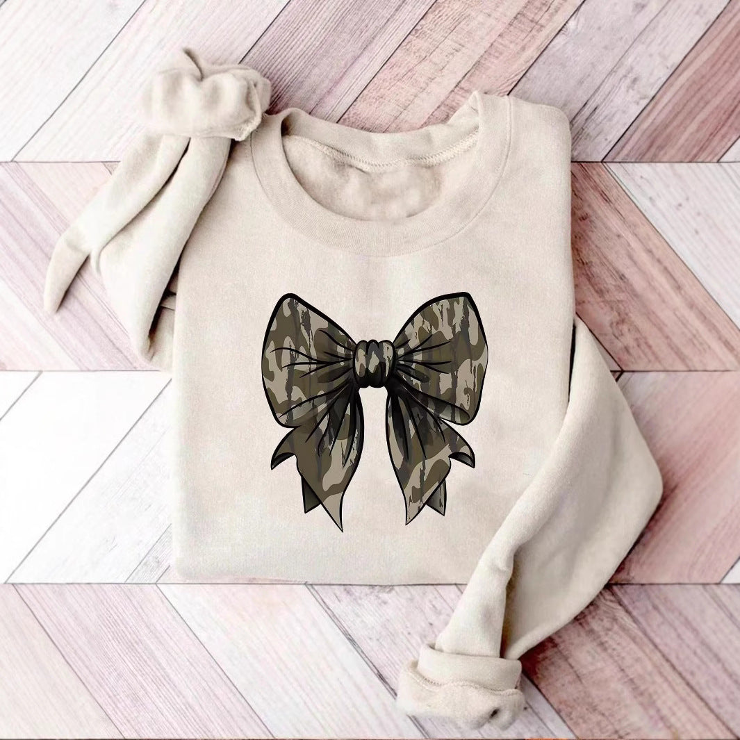 Beiges Sweatshirt mit großem Camouflage-Schleifen-Design auf Holzfußboden. Modetrend, lässiger Stil, Damenbekleidung, urbaner Look.