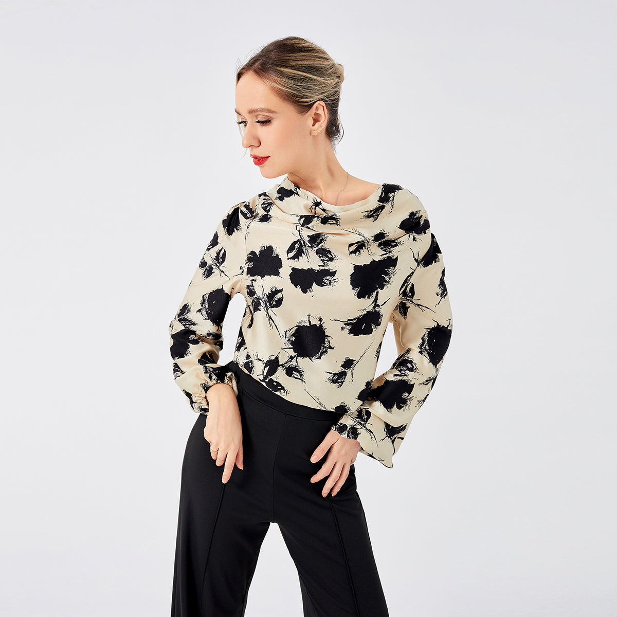 Frau in eleganter Bluse mit schwarzem Blumenmuster und schwarzer Hose vor weißem Hintergrund. Modetrend, Damenmode, stilvolle Kleidung.