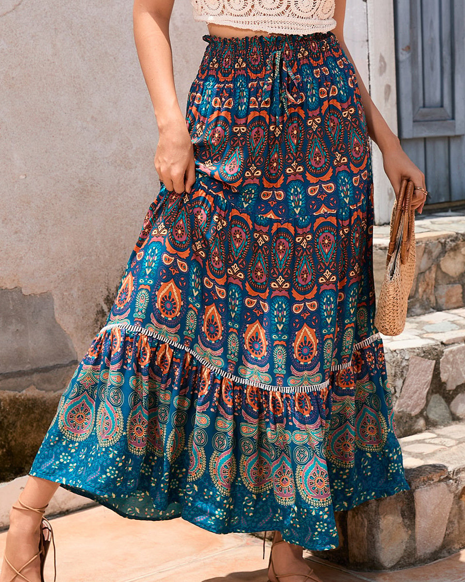 Frau in langem, blauem Boho-Rock mit Paisley-Muster, hält eine Strohtasche. Sommermode, Boho-Chic, Damenbekleidung, lässiger Stil.