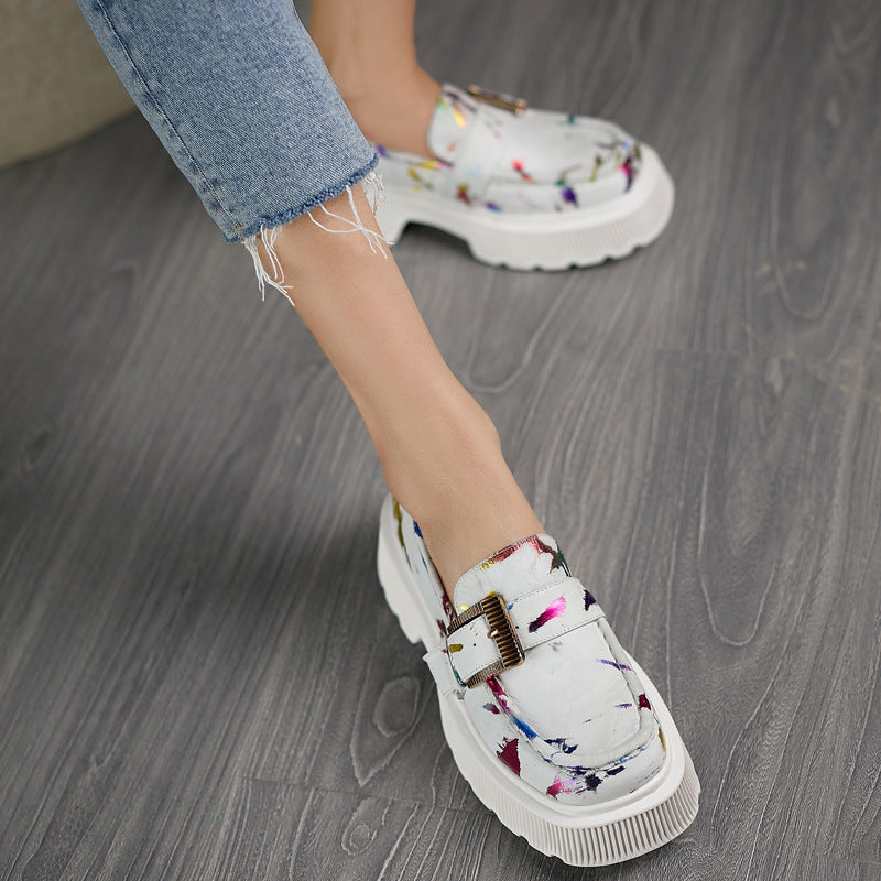 Damen-Sneaker mit weißem, gemustertem Obermaterial und dicker Sohle, kombiniert mit blauer Jeans auf grauem Holzboden. Modische Freizeitschuhe.