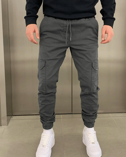 Graue Cargo-Jogginghose für Herren, kombiniert mit weißen Sneakers. Bequeme Freizeitmode, ideal für sportliche und lässige Outfits.
