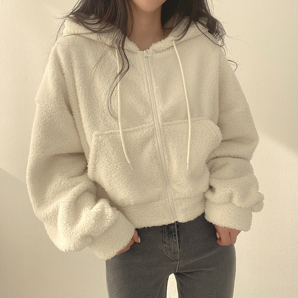 Frau trägt weiße Teddy-Fleece-Jacke mit Kapuze und Reißverschluss, kombiniert mit grauen Jeans. Wintermode, gemütlicher Stil, Damenbekleidung.