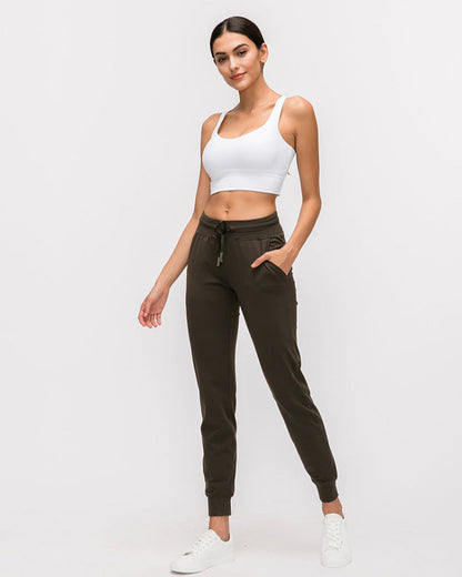 Frau in weißem Sport-BH und olivgrüner Jogginghose, lässige Sportbekleidung, Mode für Damen, bequeme Freizeitkleidung, weiße Sneaker.