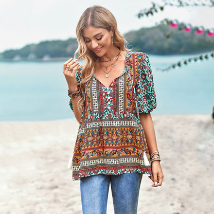 Junge Frau am Strand in bunter Boho-Bluse und Jeans, lächelnd. Sommermode, Strandkleidung, Boho-Stil, Freizeitlook.