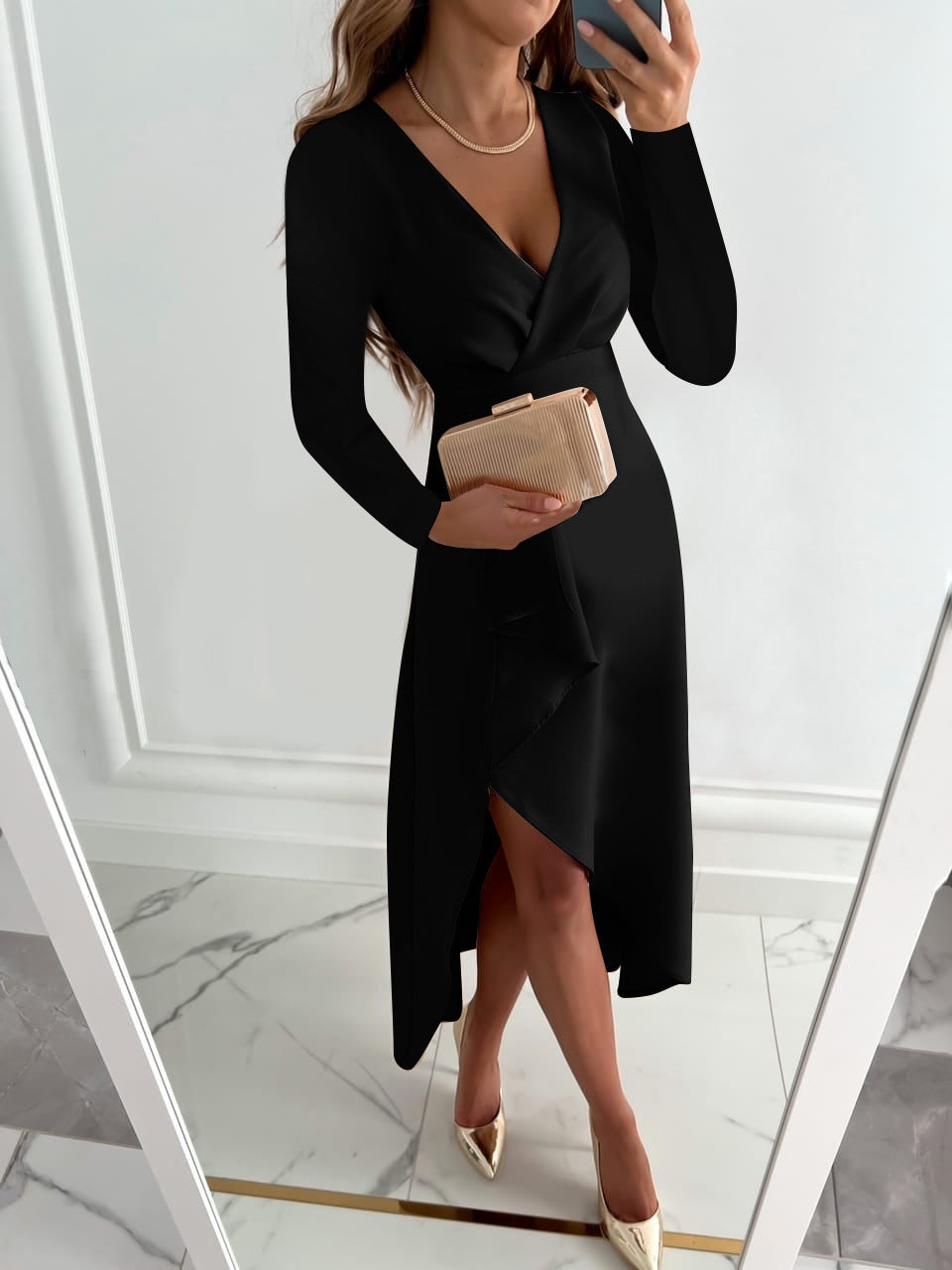 Frau im eleganten schwarzen Kleid mit V-Ausschnitt, hält eine beige Clutch, trägt goldene Schuhe, steht vor einem Spiegel. Perfekt für Abendmode.