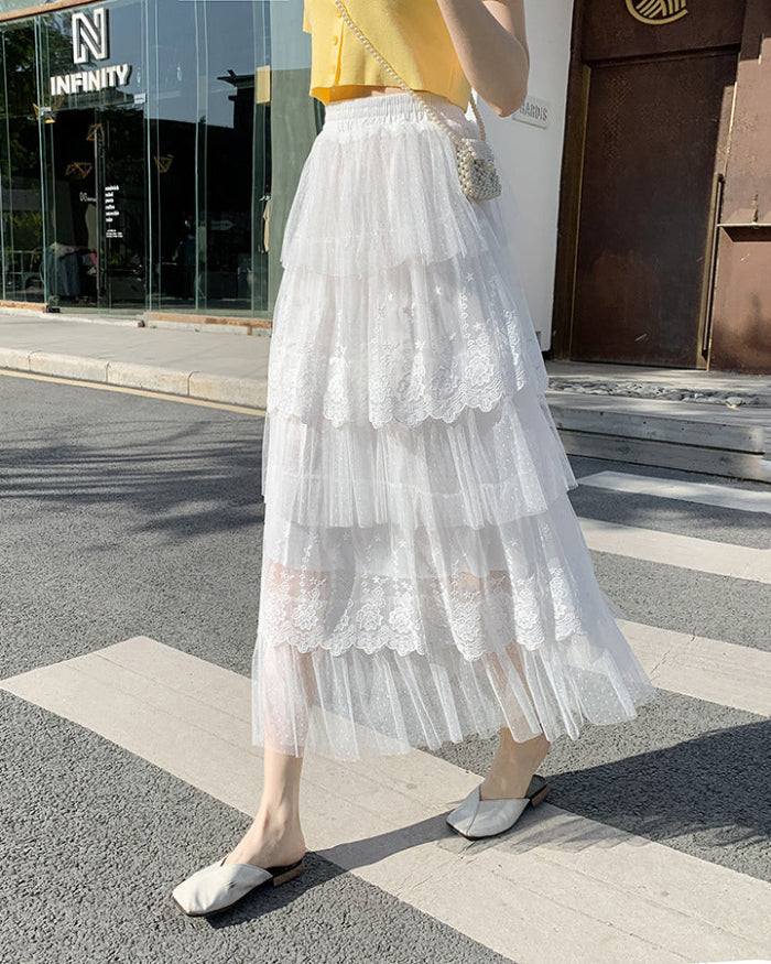 Frau in weißem, mehrlagigem Tüllrock mit Spitzenbesatz, gelbem Oberteil und flachen Schuhen überquert Straße. Sommermode, eleganter Stil.