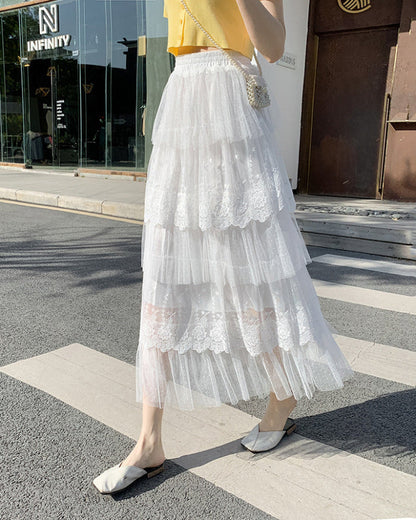 Frau in weißem, mehrlagigem Tüllrock mit Spitzenbesatz, gelbem Oberteil und flachen Schuhen überquert Straße. Sommermode, eleganter Stil.