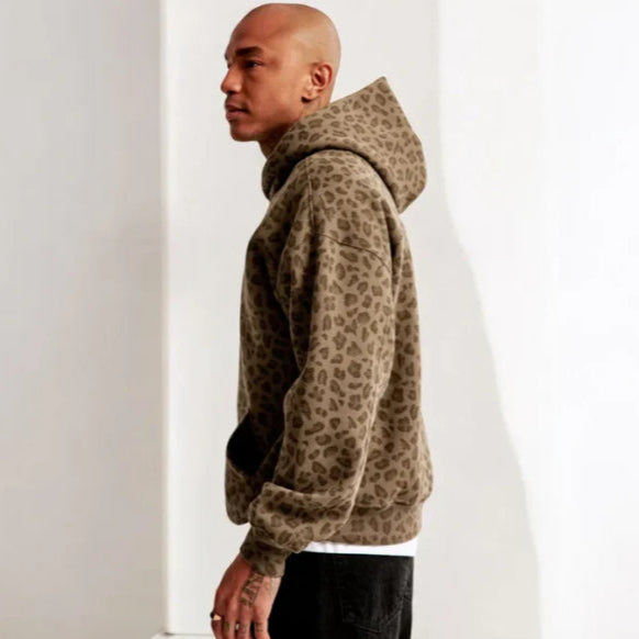 Mann in braunem Leopardenmuster-Hoodie, seitlich stehend vor weißem Hintergrund. Modetrend, Streetwear, Herrenmode, lässiger Stil.