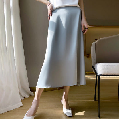 Eleganter grauer Maxirock aus Satin, kombiniert mit weißen Pumps und einem weißen Oberteil, in modernem, minimalistischem Interieur.