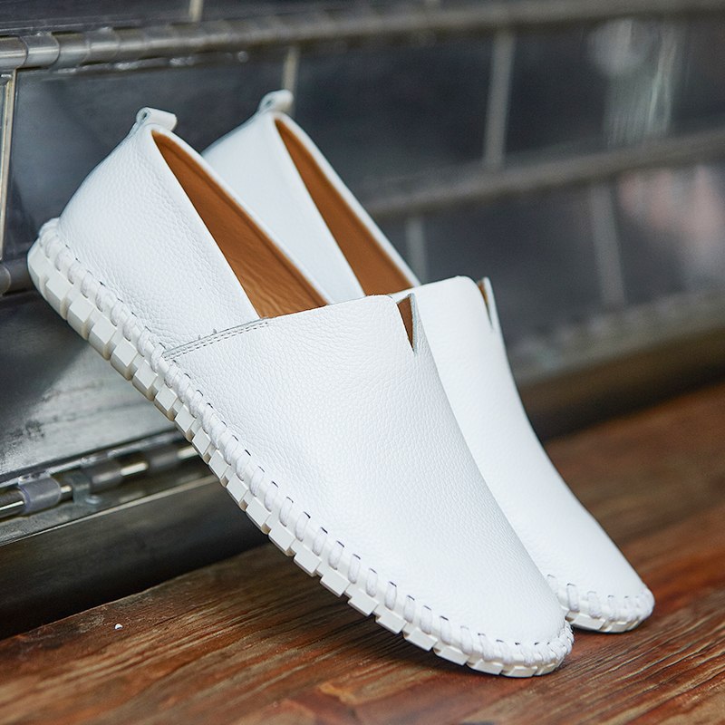 Weiße Lederschuhe für Herren, lässig und modern, auf Holzboden. Bequeme Slipper mit genähter Sohle, ideal für Sommermode und Freizeitkleidung.