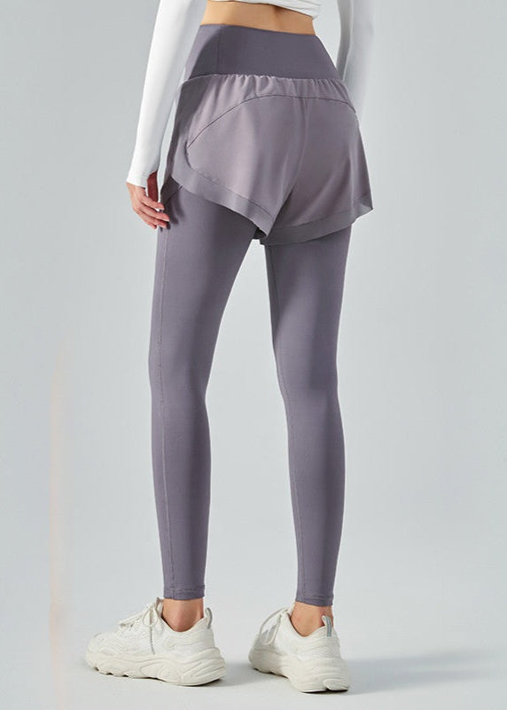 Frau in grauen Leggings mit Shorts, weißem Langarmshirt und weißen Sneakers. Sportbekleidung, Fitnessmode, bequeme Damenoutfits.