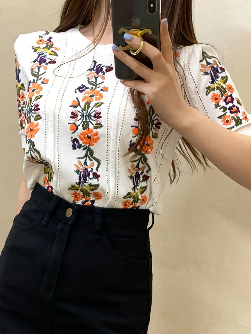Frau trägt weißes T-Shirt mit buntem Blumenmuster, fotografiert im Spiegel. Modetrend, florales Design, Sommeroutfit, stilvolle Damenmode.
