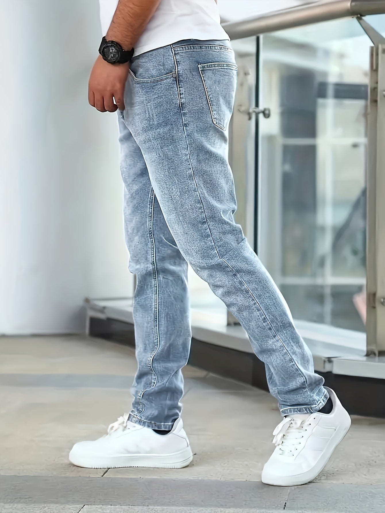 Mann in hellblauer Jeans und weißen Sneakers, seitlich stehend. Moderne Herrenmode, lässiger Stil, urbaner Look, modische Freizeitkleidung.