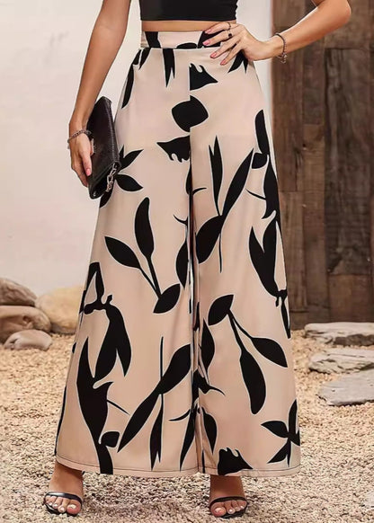 Damenhose mit weitem Bein, beige mit schwarzem Blattmuster, kombiniert mit schwarzem Top und Sandalen. Elegante Sommermode, stilvoll und modern.