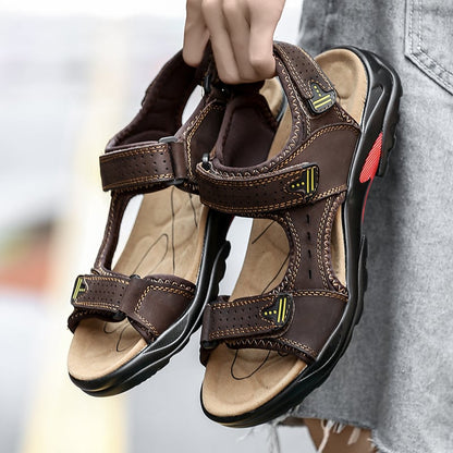 Braune Ledersandalen mit Klettverschluss, ergonomischer Sohle und roten Akzenten, in Hand gehalten. Ideal für Outdoor-Aktivitäten und Sommermode.