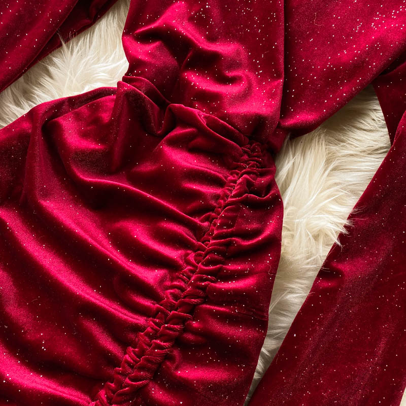 Rotes Samtkleid mit Raffung und Glitzer auf weißem Fellhintergrund. Elegantes Abendkleid, glamouröse Mode, luxuriöser Stoff.