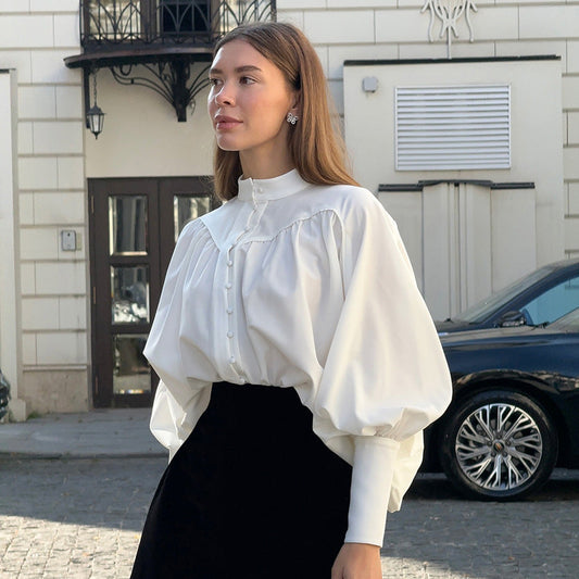 Frau in eleganter weißer Bluse mit Puffärmeln steht vor einem Gebäude. Modetrend, stilvolle Damenmode, zeitlose Eleganz, urbane Kulisse.