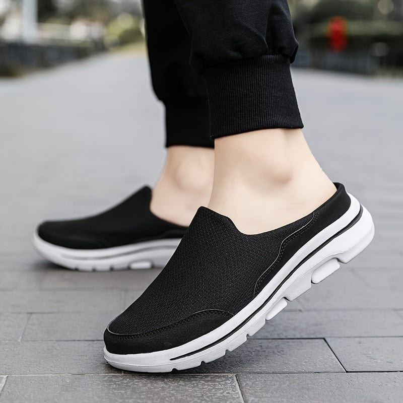 Schwarze Herren-Sneaker ohne Schnürsenkel, atmungsaktiv, mit weißer Sohle, ideal für Freizeit und Sport, auf grauem Gehweg getragen.