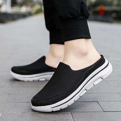 Schwarze Herren-Sneaker ohne Schnürsenkel, atmungsaktiv, mit weißer Sohle, ideal für Freizeit und Sport, auf grauem Gehweg getragen.