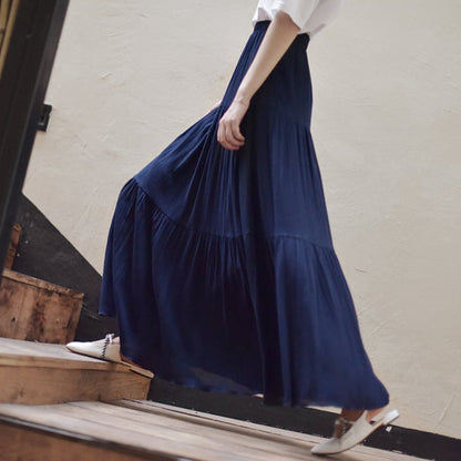 Frau in langem, fließendem dunkelblauem Maxirock und weißen Schuhen geht eine Holztreppe hinauf. Elegante Mode, lässiger Stil.