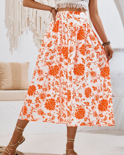 Frau in weißem, ärmellosem Oberteil und langem, orange-weiß geblümtem Rock, stehend in modernem, boho-inspiriertem Raum mit Makramee-Dekor.