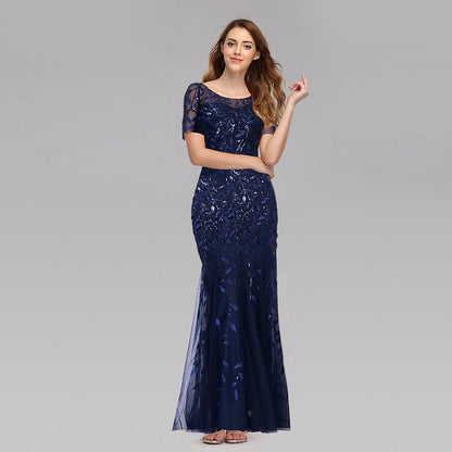Frau in elegantem, dunkelblauem Abendkleid mit Pailletten, lächelt und posiert vor grauem Hintergrund. Perfekt für Gala, Ball oder formelle Anlässe.