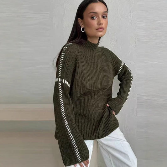 Frau in olivgrünem Strickpullover mit weißen Akzenten, sitzt vor grauer Wand. Modetrend, Herbstmode, Damenbekleidung, stilvoller Look.