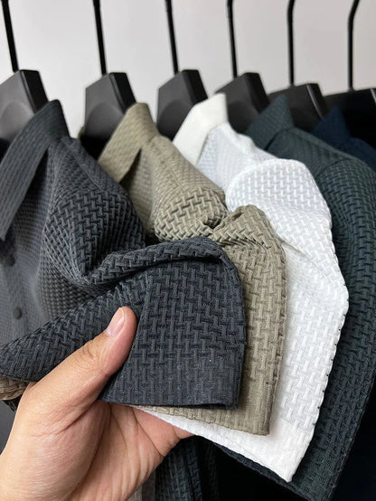 Hand hält verschiedene Hemden mit gewebter Textur in Schwarz, Beige, Weiß und Dunkelblau auf Kleiderbügeln. Hochwertige Stoffe, Mode, Textildesign.