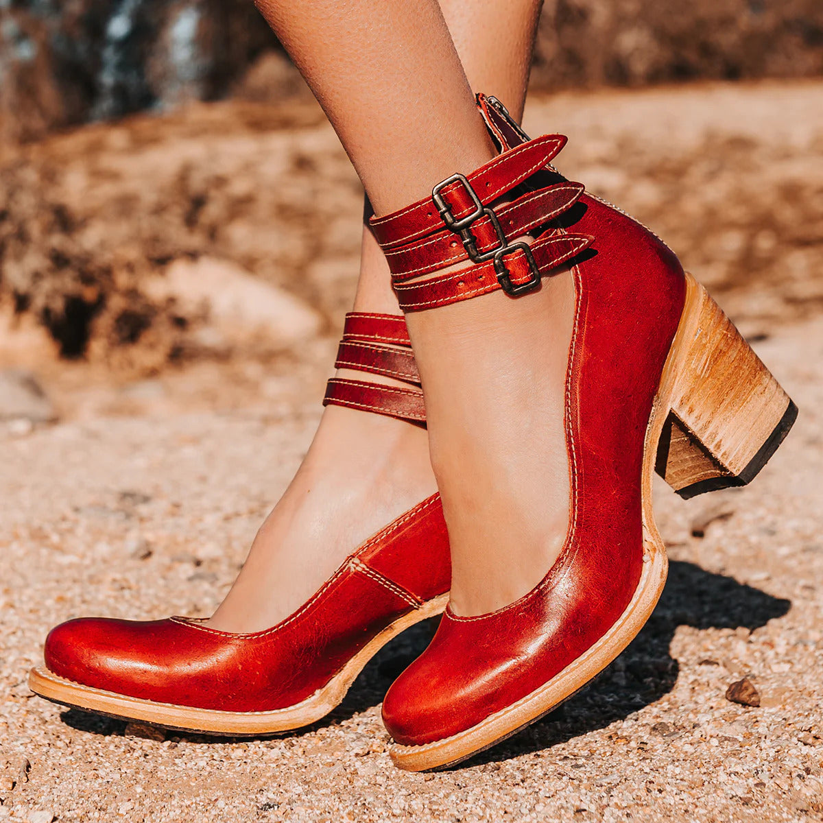 Rote Damen-Lederschuhe mit Blockabsatz und Schnallen, stilvoll auf sandigem Untergrund präsentiert. Perfekt für modische Herbst-Outfits.