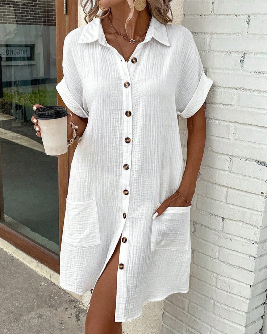 Frau in weißem Leinenhemdkleid mit Knopfleiste und Taschen, hält Kaffeebecher. Sommermode, lässiger Stil, trendiges Outfit.