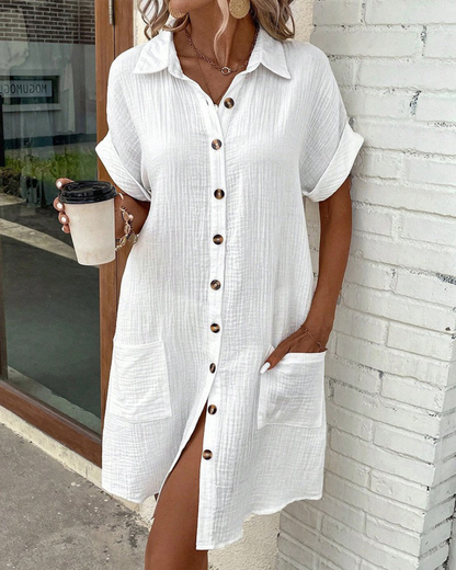 Frau in weißem Leinenhemdkleid mit Knopfleiste und Taschen, hält Kaffeebecher. Sommermode, lässiger Stil, trendiges Outfit.