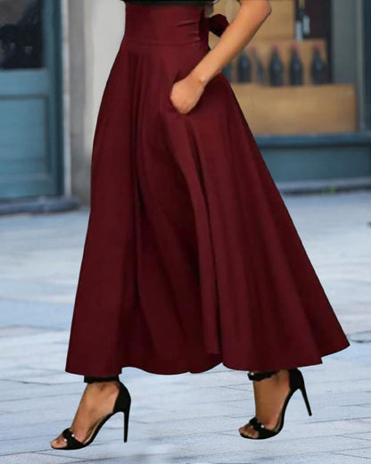 Frau in eleganter, weinroter, knöchellanger A-Linien-Rock mit Taschen, kombiniert mit schwarzen High Heels, auf städtischem Hintergrund.
