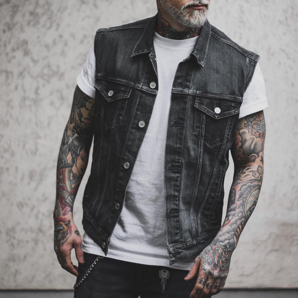 Mann mit tätowierten Armen trägt schwarze Jeansweste und weißes T-Shirt. Moderner Streetwear-Look, lässiger Stil, Mode für Männer.