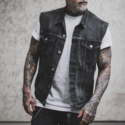 Mann mit tätowierten Armen trägt schwarze Jeansweste und weißes T-Shirt. Moderner Streetwear-Look, lässiger Stil, Mode für Männer.