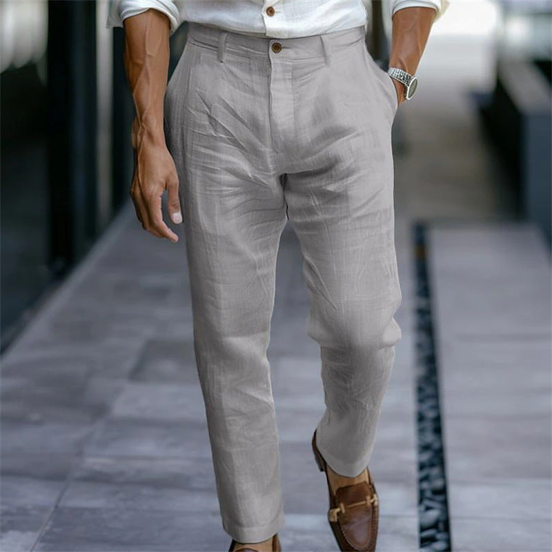 Mann in eleganter, grauer Leinenhose und braunen Loafern, gehend auf modernem Gehweg. Stilvolle Herrenmode, Freizeitlook, Sommeroutfit.