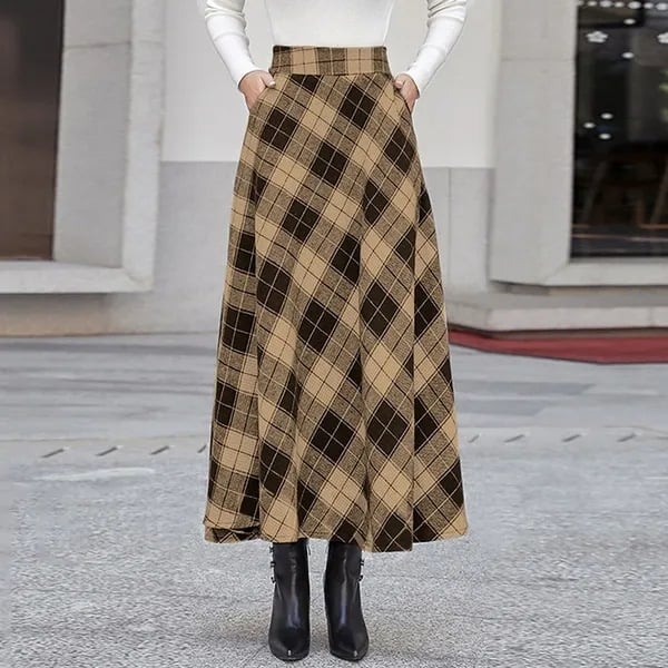 Damenmode: Langer karierter Rock in Beige und Braun, kombiniert mit weißem Oberteil und schwarzen Stiefeln. Eleganter Herbst-Look auf grauem Hintergrund.