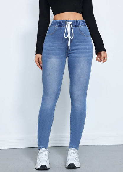 Frau trägt blaue Jeans-Leggings mit Kordelzug, kombiniert mit schwarzem Langarm-Oberteil und weißen Sneakers. Modetrend, Damenbekleidung, Freizeitlook.