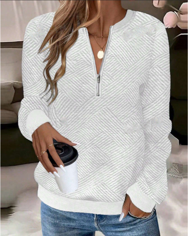 Frau in weißem Strickpullover mit Reißverschluss hält Kaffeebecher. Modischer Freizeitlook, ideal für Herbst und Winter.
